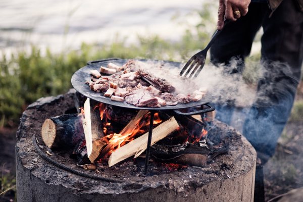 En man steker kött över en grillplats i naturen.