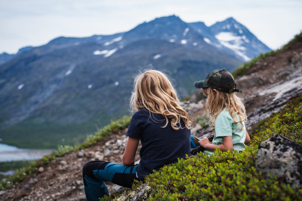 Två barn sitter på en sluttning i ett naturområde.